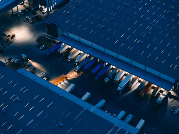 Aerial view of semi-trucks lined up at warehouse loading docks in distribution center parking lot at dusk