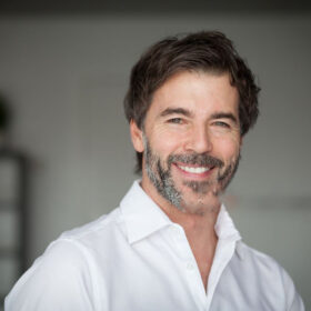 Alt Text: "Professional middle-aged businessman in white shirt smiling confidently in modern office